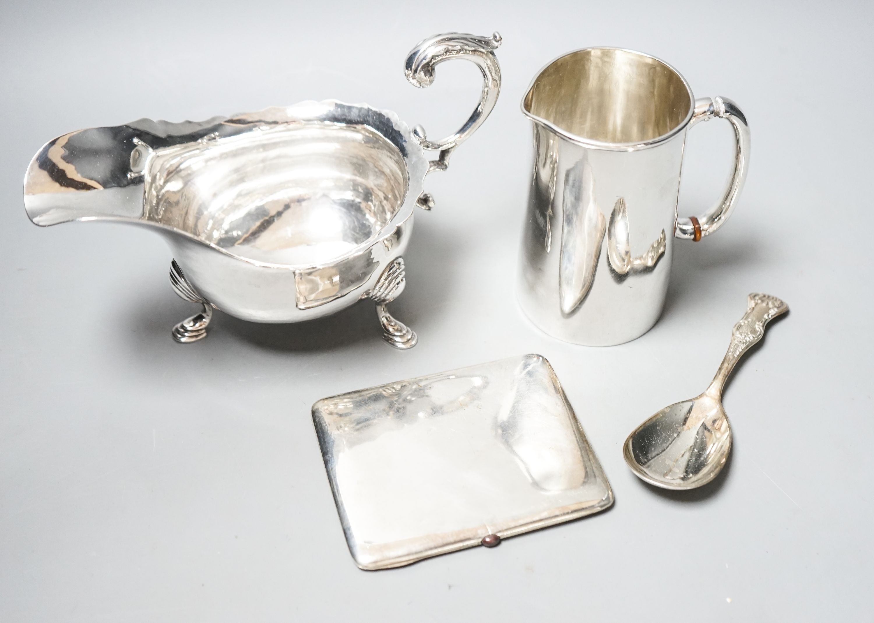 A George V silver sauceboat, a silver jug with military related inscription, a silver cigarette case and silver spoon